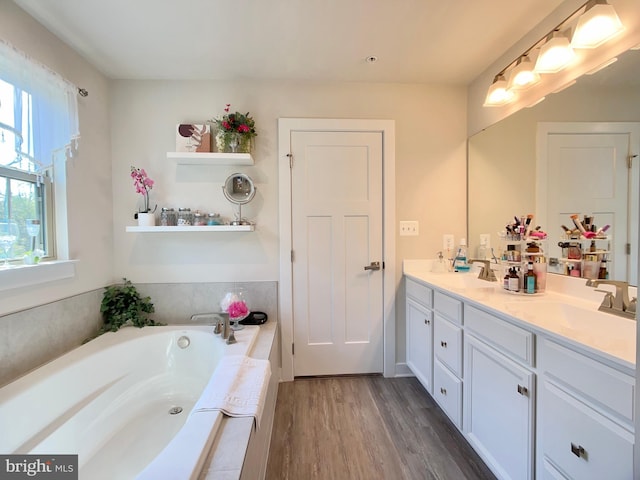 full bathroom with double vanity, wood finished floors, a bath, and a sink