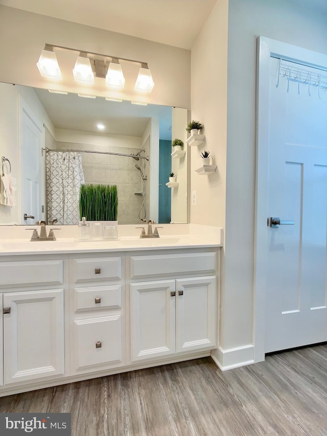 bathroom featuring double vanity, wood finished floors, a shower, and a sink