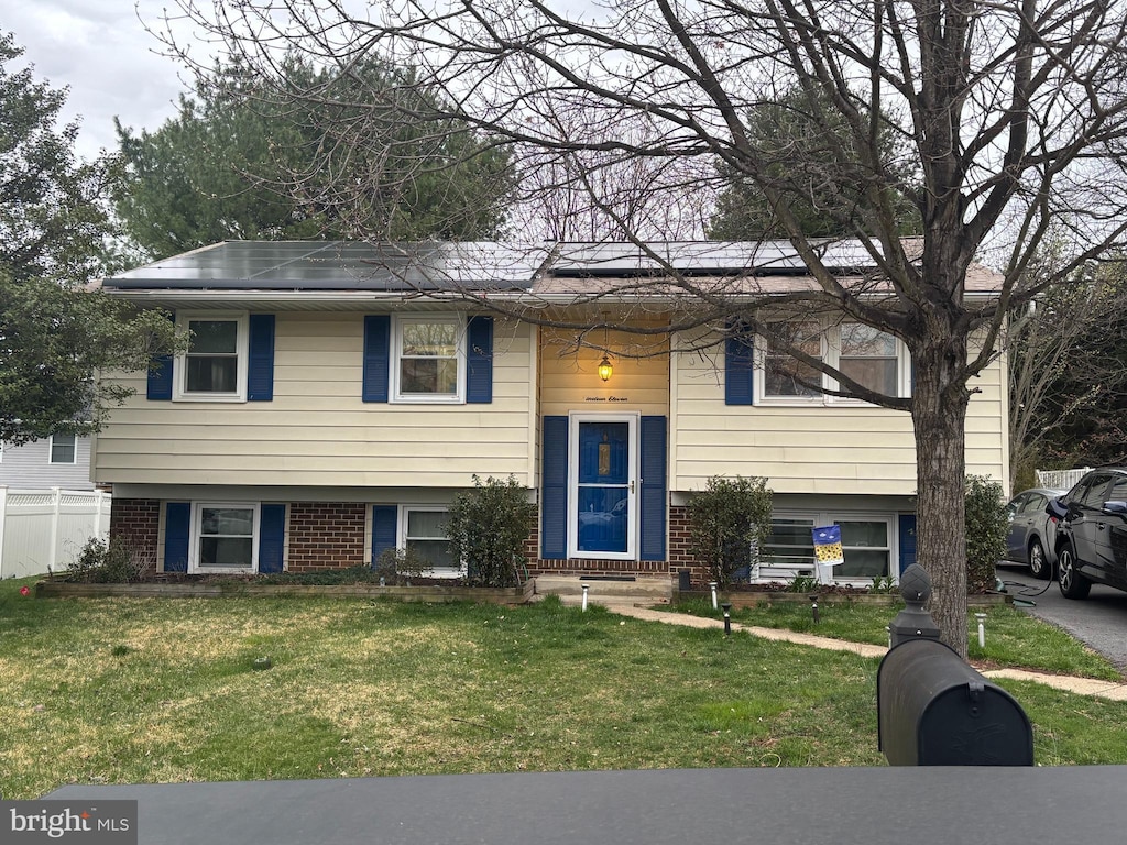 split foyer home featuring a front lawn, brick siding, and solar panels