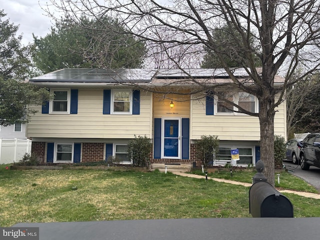 split foyer home featuring a front lawn, brick siding, and solar panels