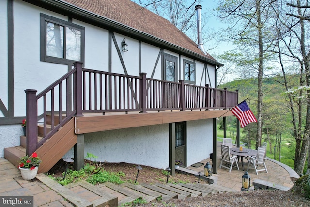 rear view of house featuring a patio area, roof with shingles, and stucco siding