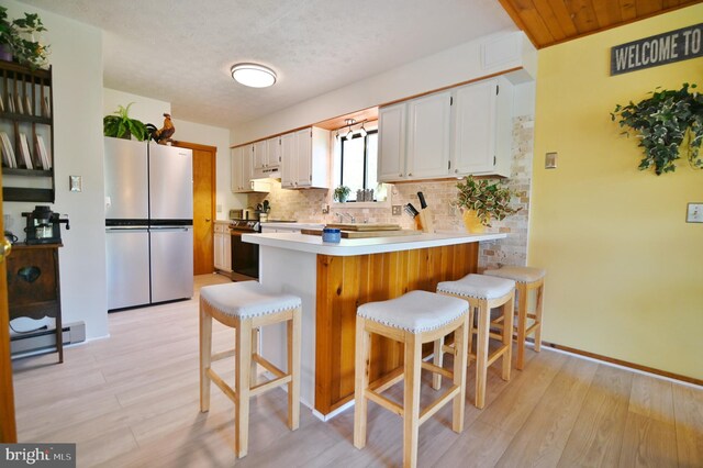 kitchen with decorative backsplash, stove, a baseboard radiator, freestanding refrigerator, and a peninsula