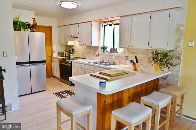 kitchen featuring freestanding refrigerator, electric range, a peninsula, under cabinet range hood, and backsplash