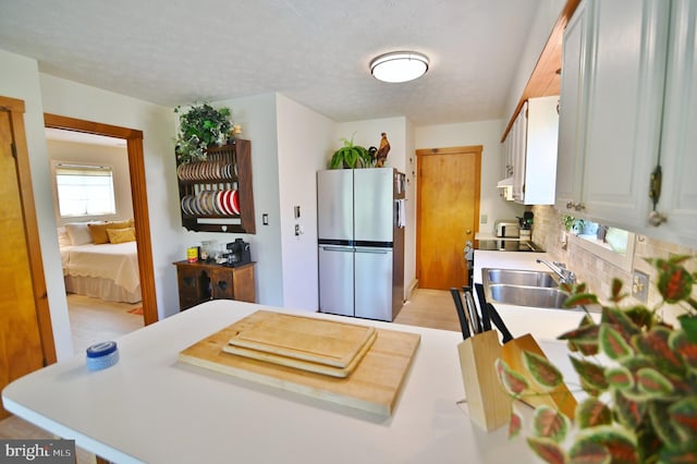 kitchen featuring a sink, light countertops, tasteful backsplash, and freestanding refrigerator