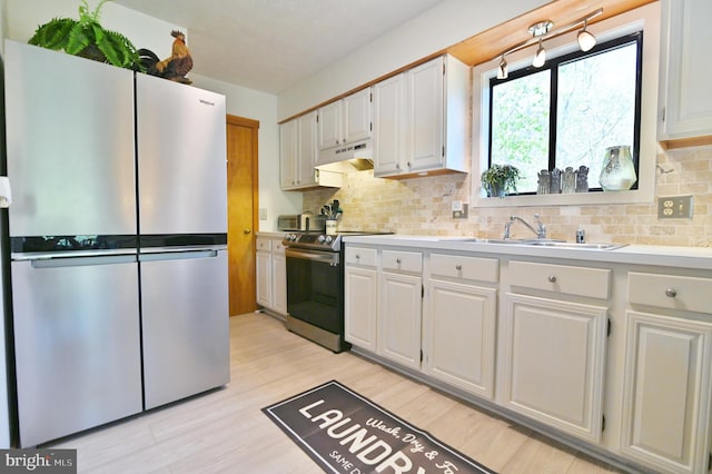 kitchen with light countertops, under cabinet range hood, tasteful backsplash, a sink, and stainless steel appliances