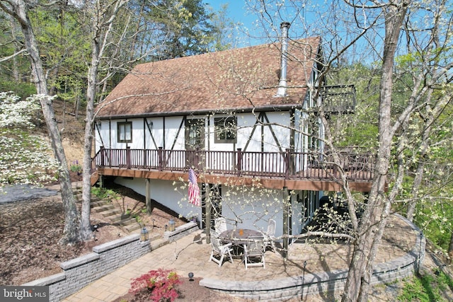 rear view of property featuring a patio, a shingled roof, a wooden deck, and stucco siding