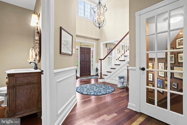 foyer entrance featuring wainscoting, a decorative wall, dark wood-style flooring, and a chandelier