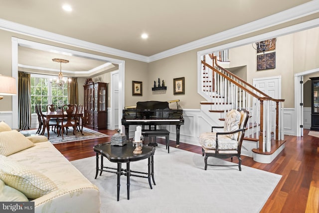 living area featuring crown molding, a notable chandelier, wainscoting, wood finished floors, and stairway