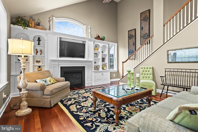 living room with a fireplace with flush hearth, wood finished floors, stairway, high vaulted ceiling, and baseboards