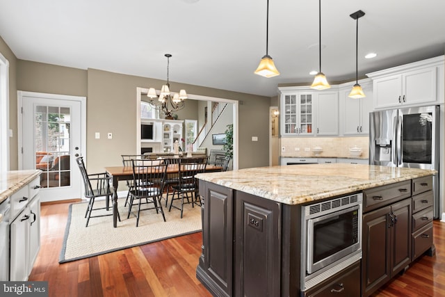 kitchen with backsplash, appliances with stainless steel finishes, wood finished floors, white cabinets, and an inviting chandelier