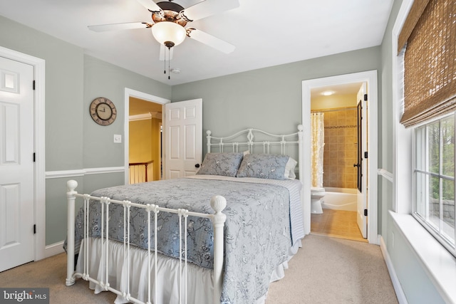 bedroom featuring baseboards, ensuite bathroom, light carpet, and a ceiling fan