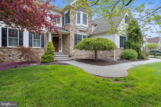 traditional home featuring roof with shingles, stucco siding, a front yard, and stone siding