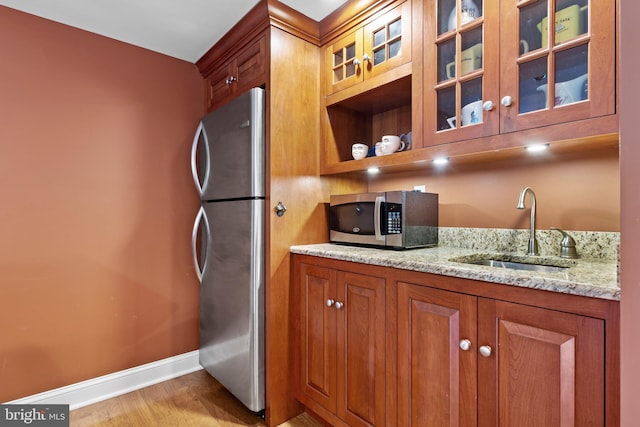 kitchen featuring brown cabinets, appliances with stainless steel finishes, light stone counters, a sink, and baseboards