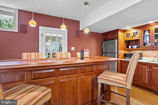 bar with a sink, hanging light fixtures, a bar, and light wood finished floors