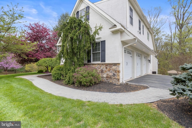view of home's exterior featuring driveway, a yard, an attached garage, stone siding, and stucco siding