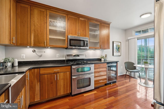 1617 Potomac Greens Dr Unit A, Alexandria, VA 22314 - kitchen featuring appliances with stainless steel finishes, beverage cooler, brown cabinetry, wood finished floors, and glass insert cabinets