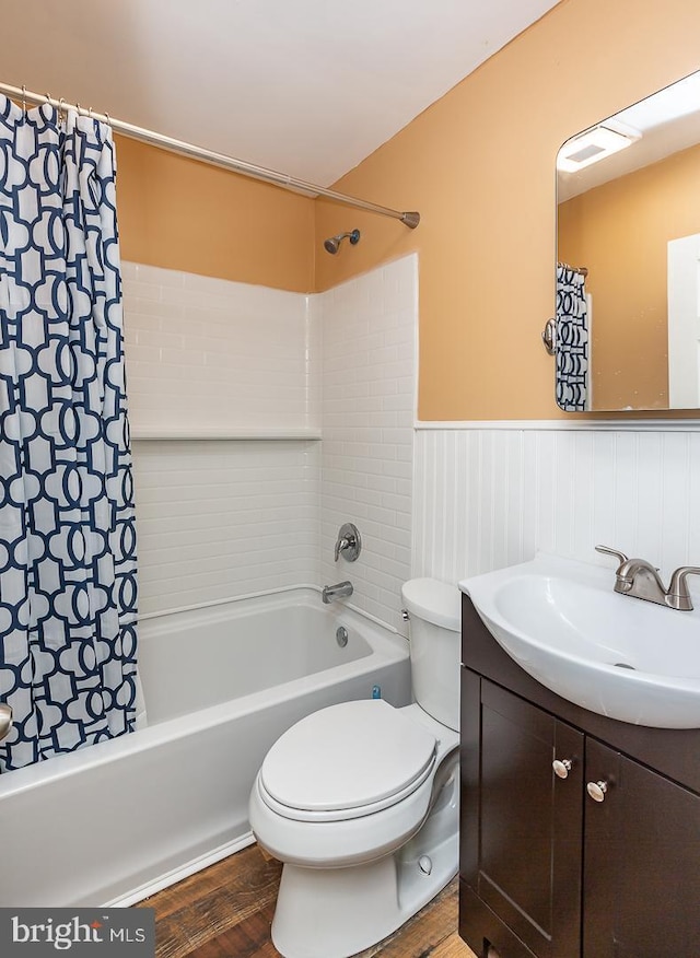 full bath with shower / bath combo, a wainscoted wall, toilet, wood finished floors, and vanity