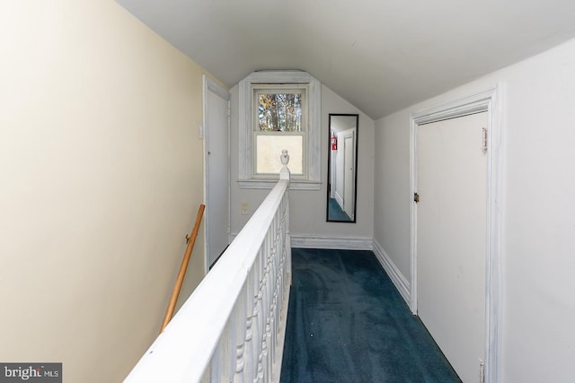 corridor featuring dark colored carpet, lofted ceiling, baseboards, and an upstairs landing