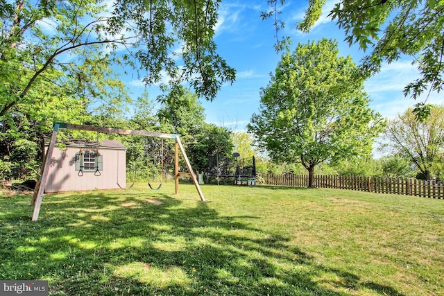 view of yard with fence, a shed, a playground, a trampoline, and an outbuilding