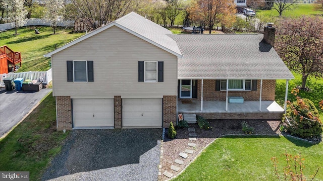 split level home with an attached garage, a chimney, a porch, and brick siding