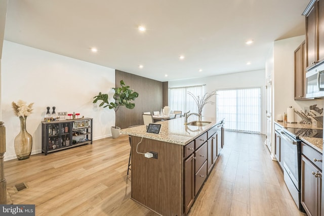 kitchen featuring visible vents, a center island with sink, stainless steel microwave, electric stove, and light wood-style flooring