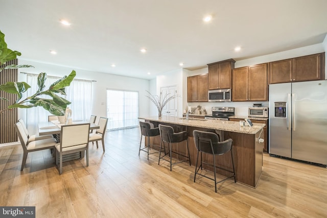 kitchen featuring a kitchen island with sink, a breakfast bar, light stone counters, light wood-style flooring, and stainless steel appliances
