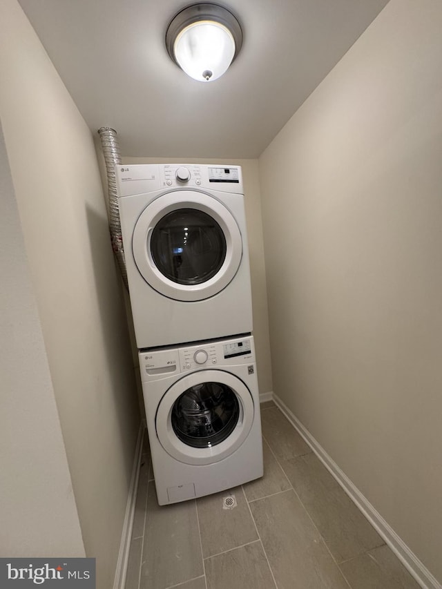 laundry area featuring baseboards, stacked washer and dryer, tile patterned floors, and laundry area