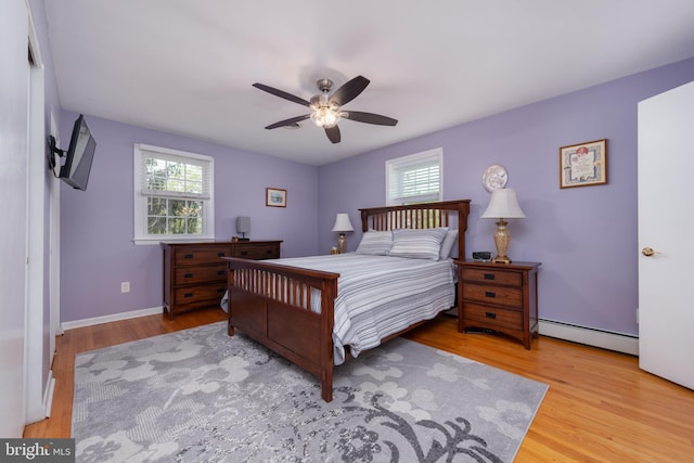 bedroom with wood finished floors, a ceiling fan, baseboard heating, and multiple windows