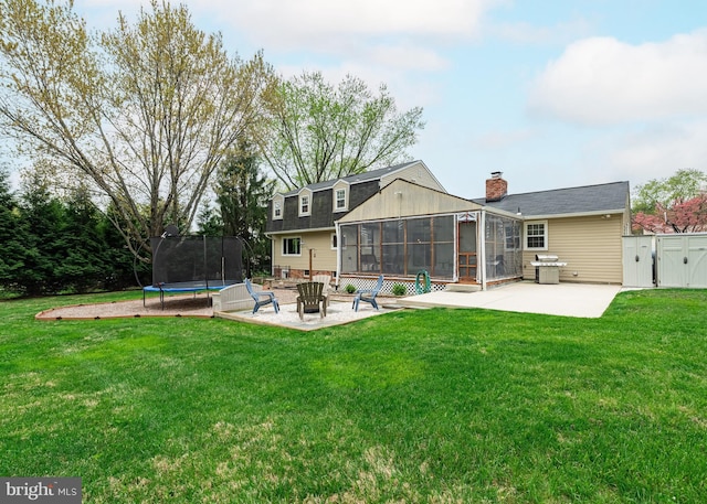 rear view of house with a chimney, a patio, a lawn, a sunroom, and a trampoline