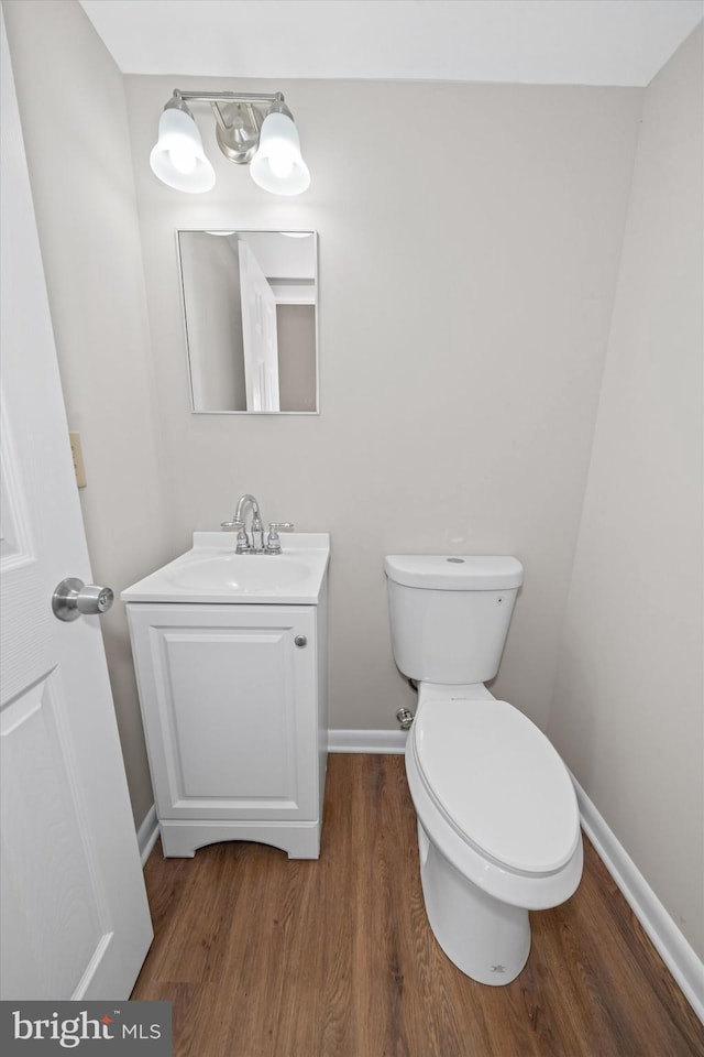 half bathroom featuring baseboards, wood finished floors, vanity, and toilet
