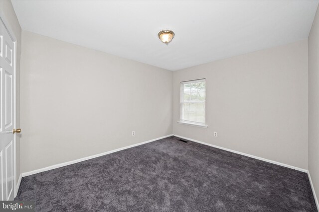 empty room featuring dark colored carpet, visible vents, and baseboards
