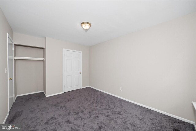 unfurnished bedroom with baseboards, dark colored carpet, and a closet