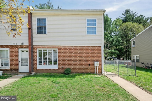 rear view of property with a gate, brick siding, fence, and a yard