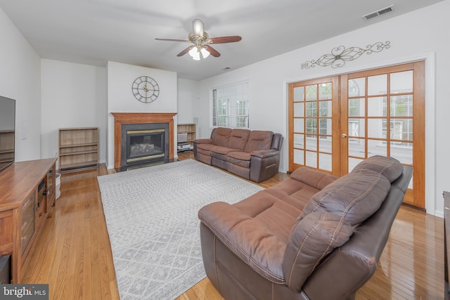 living room featuring visible vents, light wood finished floors, ceiling fan, and a glass covered fireplace