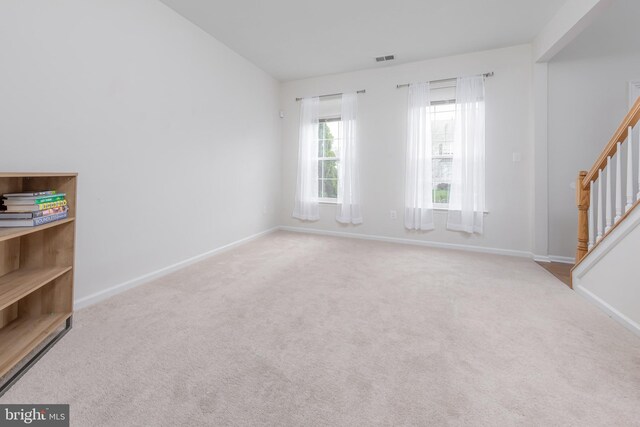 carpeted spare room featuring stairway, baseboards, and visible vents