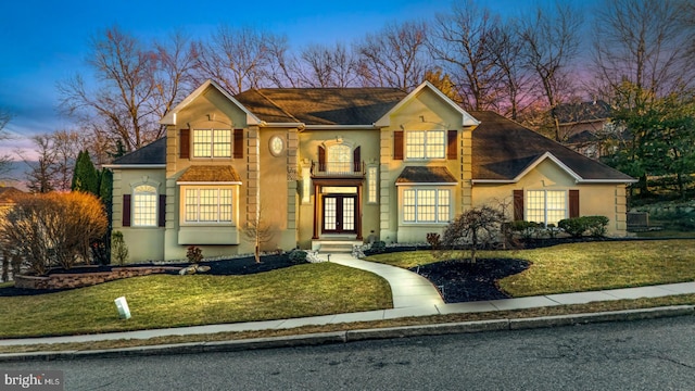 traditional-style house featuring stucco siding, a lawn, and french doors