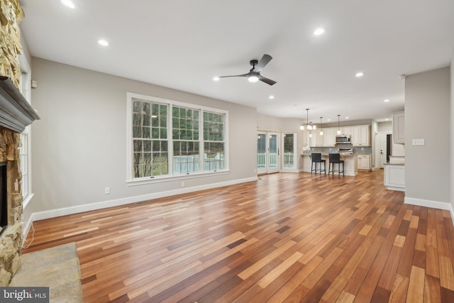 unfurnished living room featuring baseboards, recessed lighting, light wood-style floors, ceiling fan, and a stone fireplace