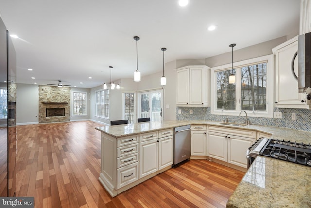 kitchen featuring light wood finished floors, a peninsula, a sink, and appliances with stainless steel finishes