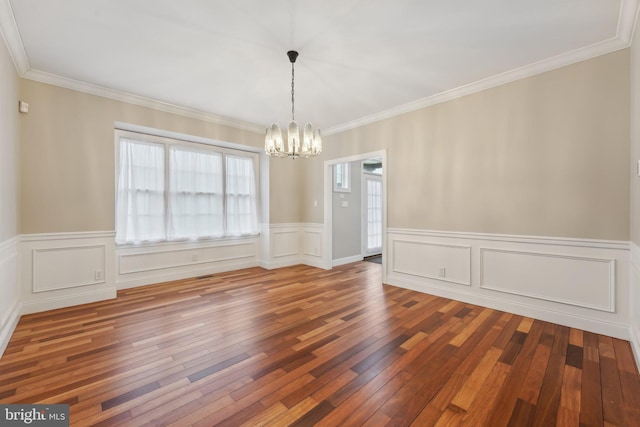 unfurnished dining area featuring wainscoting, wood-type flooring, an inviting chandelier, and ornamental molding