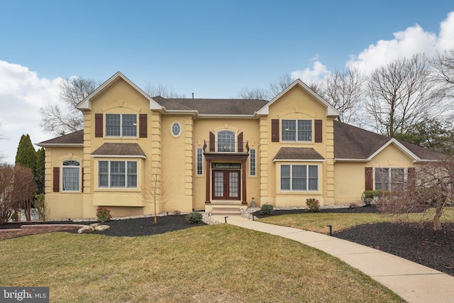 traditional-style house with a shingled roof, a front lawn, a balcony, stucco siding, and french doors