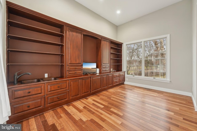 unfurnished office featuring baseboards, a sink, visible vents, and light wood-type flooring