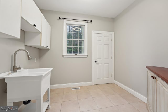 laundry area with baseboards, light tile patterned flooring, and a sink