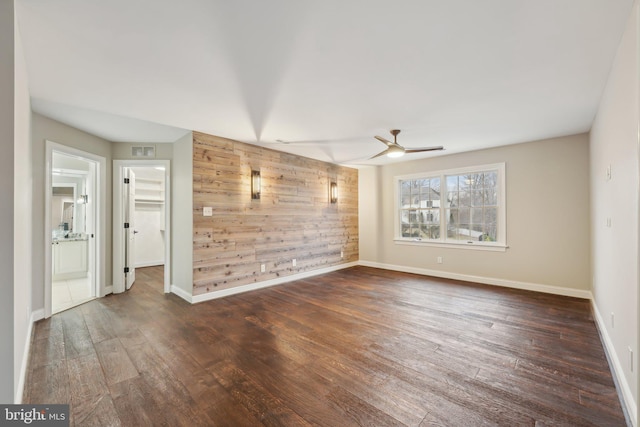 empty room with wood walls, wood finished floors, visible vents, a ceiling fan, and baseboards