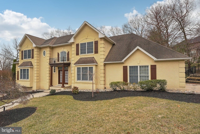 traditional-style house featuring stucco siding, a balcony, a shingled roof, and a front yard