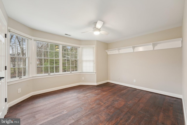 spare room featuring dark wood-type flooring, visible vents, a ceiling fan, and baseboards