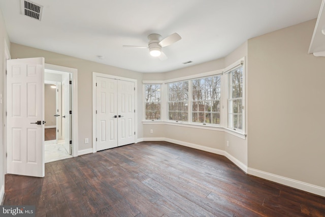 unfurnished bedroom with dark wood-type flooring, a closet, visible vents, and baseboards