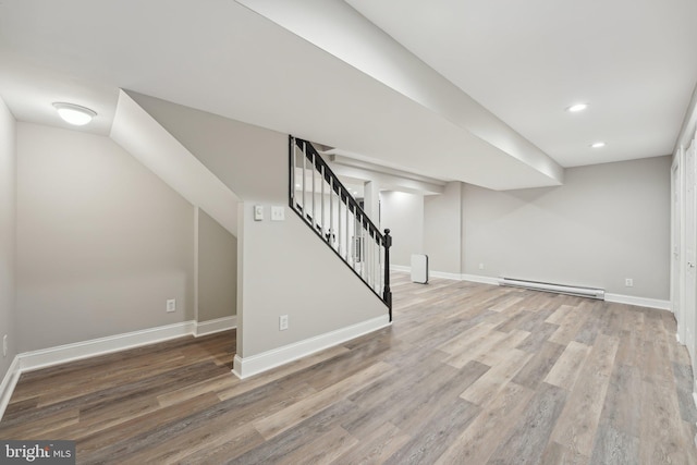 finished basement featuring a baseboard radiator, wood finished floors, stairs, baseboards, and recessed lighting