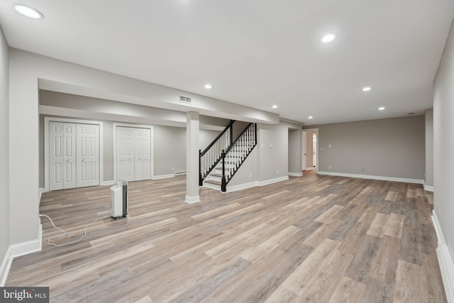 finished below grade area with light wood-type flooring, baseboards, visible vents, recessed lighting, and stairway