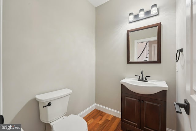 half bath with baseboards, wood finished floors, vanity, and toilet