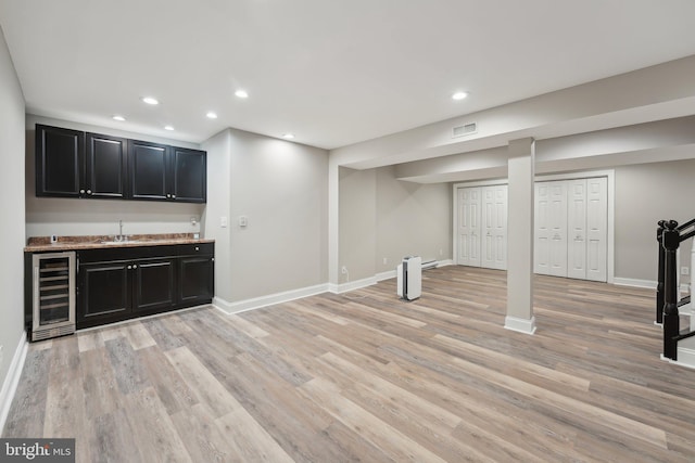finished basement with baseboards, wet bar, wine cooler, and light wood-type flooring